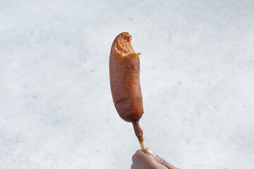 A view of a hand holding a bitten corn dog.