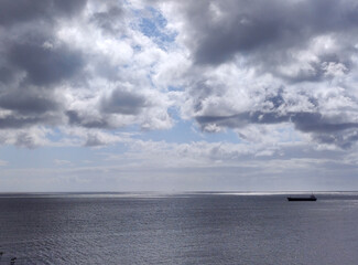 Cargo ship in the open sea. White clouds over a stormy sky background and sea