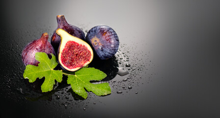 Fig fruits. Ripe sweet fresh figs fruit with leaves close up, on black background with water drops. 