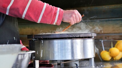 Cooking crepes at an outdoors event catering vendor, hand spreading pancake batter onto hotplate...