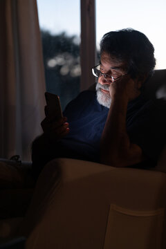 Mature latin man in dark room looking at his phone