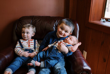 little boys meeting their newborn baby brother in home on couch