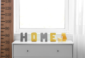 Jug with glass of juice and decor on chest of drawers in children's room