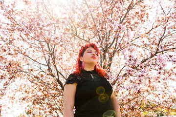Queer person posing behind almond tree in blossom with eyes closed