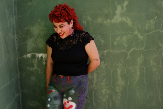 Smiling queer person with red hair over green wall
