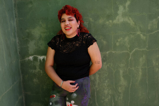 Smiling queer person with red hair over green wall