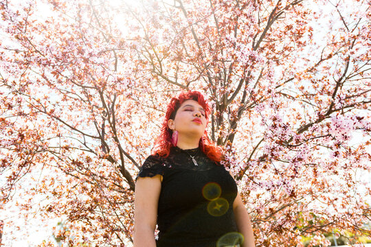 Queer person posing behind almond tree in blossom with eyes closed