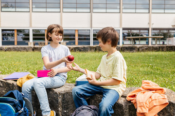 Children sit on in the school yard and eat apples and sandwiches. Snack during break time during class