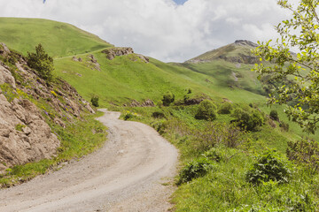 Dangerous M-20 dirt gravel road to Tskhratskaro Pass, Georgia, with Trialeti (Caucasus) green mountains landscape. Bakuriani ski lift station and South Caucasus Pipeline (SCP) in the distance.