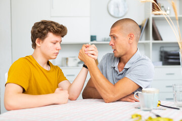 Happy smiling father and son arm wrestling at home. Fatherhood concept