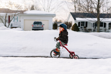 Child rides bike down snowy sidewalk