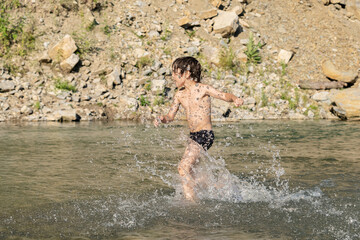 A happy boy is runs in a mountain river. He makes a lot of splashes