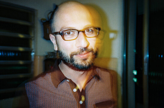 Direct flash shaky portrait of a bold man with black beard and glasses