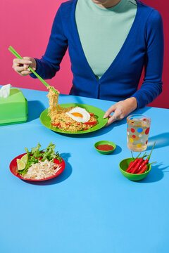 young woman eating instant noodles over color background