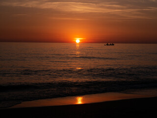 Fototapeta premium Sunset in Italy Toskana at mittelmeer with fishing boat in the water and small Waves Dawn