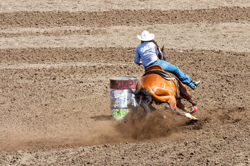Cowgirl riding in a barrel racing completion at a rodeo. She is wearing blue shirt and blue jeans...