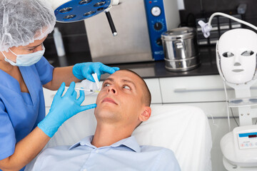 Handsome young man receiving procedure of injection contouring for facial correction in cosmetology clinic