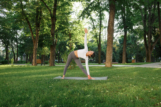 Flexible woman performing Trikonasana in park - Powered by Adobe