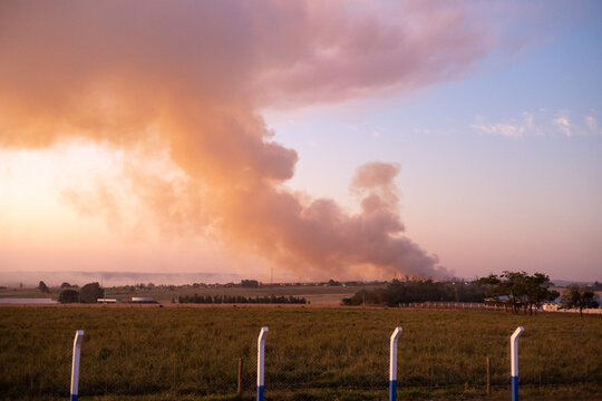 Thick colourful smoke in the sky during fire in farm with white fence 