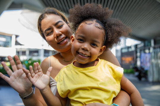 Cheerful mother with daughter waving hand and greeting to the camera