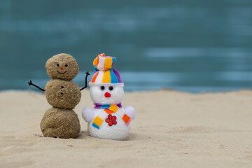 Toy snowman with sand snowman on the beach. New Year's and Christmas holiday in hot countries concept.Christmas on the beach.