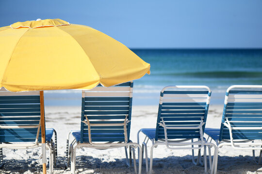 A Yellow Umbrella Next To A Row Of Blue And White Beach Chairs