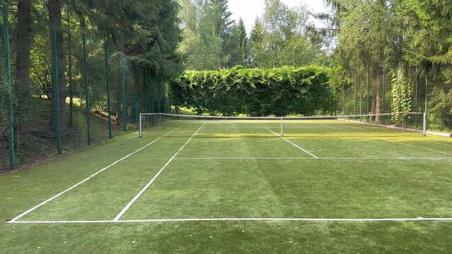 A grass tennis court in the middle of green trees and a sunny day. Grass covering of the sports field. Playing tennis.
