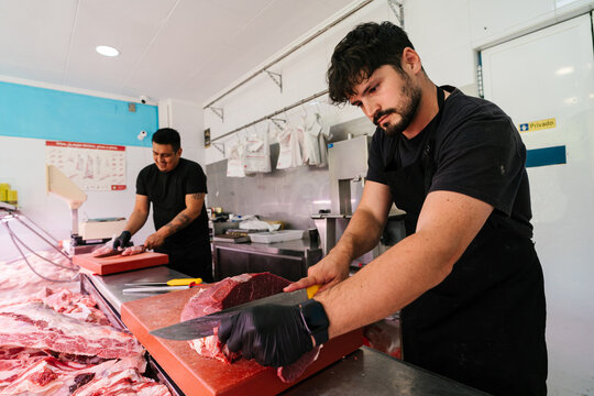 Men cutting fresh meat on wooden board in factory