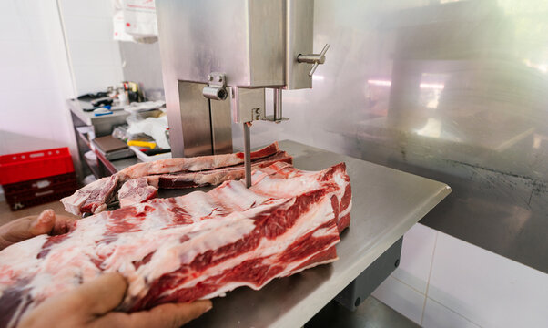Crop butcher cutting meat with band saw