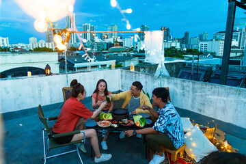 Group of Diversity Asian people friends enjoy and fun celebration meeting dinner party eating barbecue grill and drinking Korean vodka together at outdoor rooftop on summer holiday vacation at night.