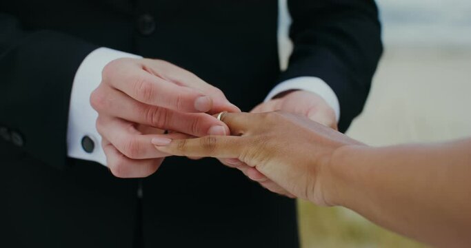 The groom puts a ring on the bride's finger, standing on the seashore, close-up of hands