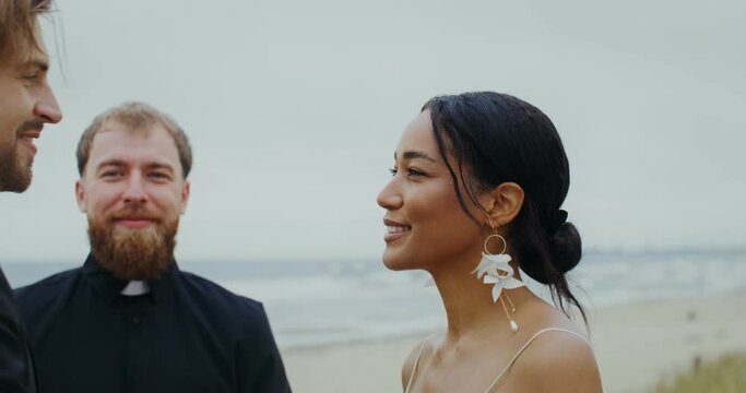 The bride and groom kiss standing in front of the priest on the seashore