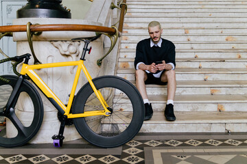 Young smiling stylish pushing bicycle while going to work
