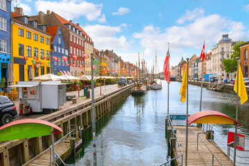 Colorful buildings with apartments, and shops alongside outdoor sidewalk cafes and docked sailboats at the 17th century Nyhavn Canal, a major tourist destination in the city of Copenhagen, Denmark. - Powered by Adobe