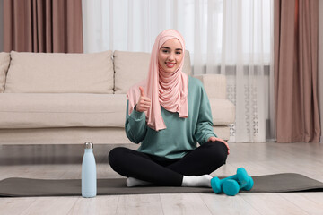 Muslim woman showing thumb up on fitness mat at home