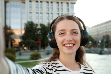 Portrait of smiling woman in headphones taking selfie on city street - obrazy, fototapety, plakaty