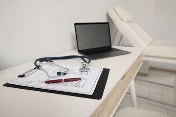 Clipboard, stethoscope, laptop and pen on white table in clinic. Doctor's workplace