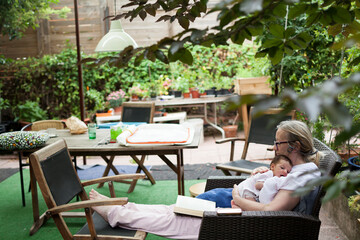 Grandma holding newborn while reading in garden
