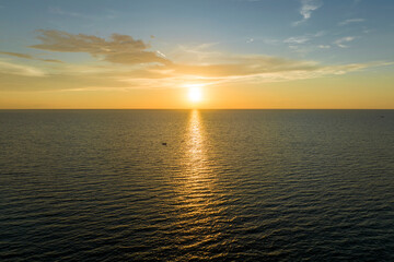 Fototapeta premium Aerial view of lonesome white yacht at sunset floating on sea waves with ripple surface. Motor boat recreation on ocean surface