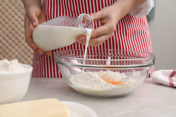 Preparing tasty baklava. Woman pouring milk into bowl with flour and eggs at light grey table, closeup