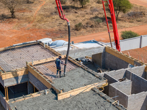 african construction workers in town at the construction site using a boom concrete pump to fill the foundation of a building