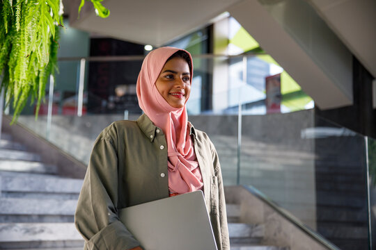 Happy arabic woman holding laptop outside office building
