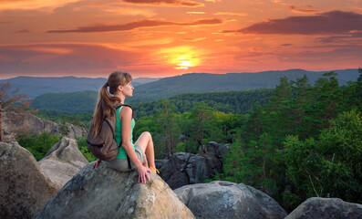 Lonely woman hiker sitting alone on rocky mountain top enjoying view of morning nature on wilderness trail. Active lifestyle concept