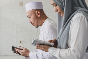 Asian muslim couple reciting Quran  in mosque during Ramadan. Couple reading holy book of Al Quran together. Selective focus.