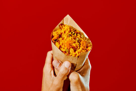 man holds a paper cone with paella