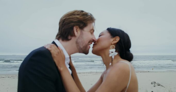 The bride and groom rub their noses and kiss standing on the seashore