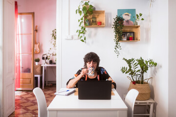 Focused woman drinking coffee using laptop at home