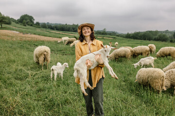 A joyful girl holds a young goat in her arms on her farm