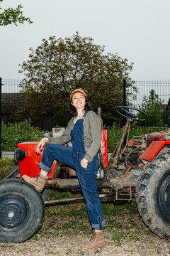 Portrait of a happy girl in work clothes with a tractor on a farm