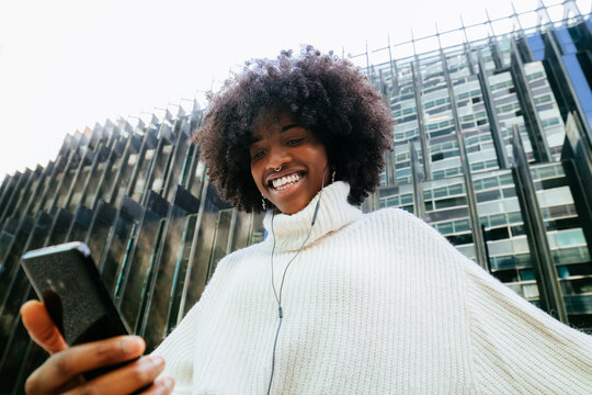 Happy black woman in earphones listening to music on smartphone
